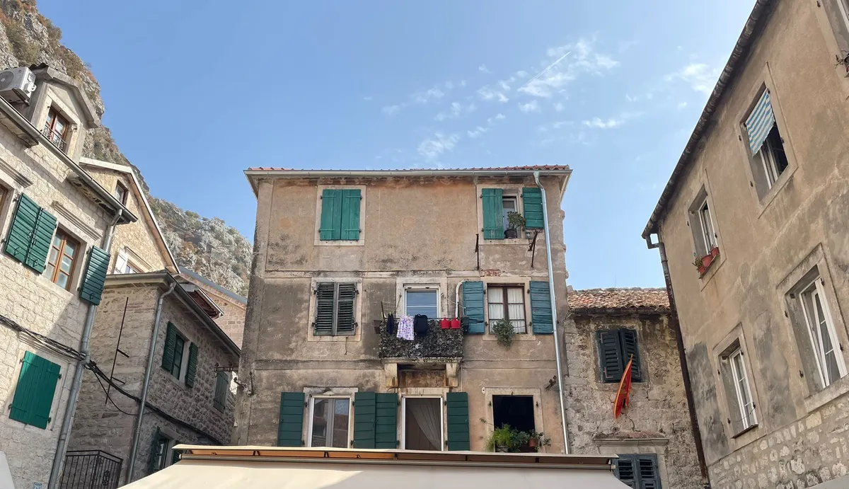 Altes Steinhaus mit grünen Fensterläden in der Altstadt von Kotor, darunter die Markise einer Konoba.