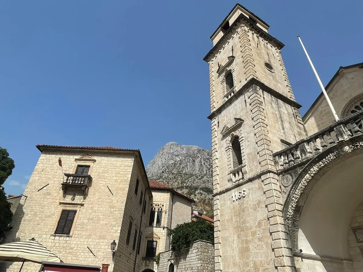 Die Kathedrale St. Tryphon in Kotor mit der Jahreszahl 1166 am Glockenturm, dahinter ein steiler Felsberg.