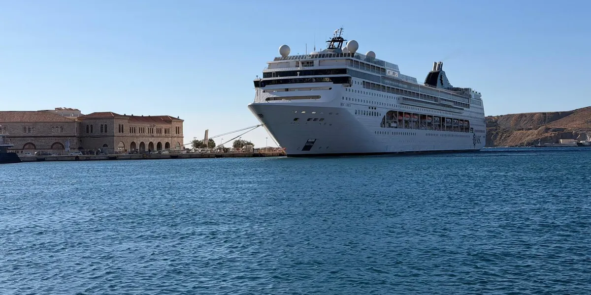 MSC Lirica ormeggiata al molo, con un vecchio edificio portuale di arenaria a sinistra e colline spoglie a destra.